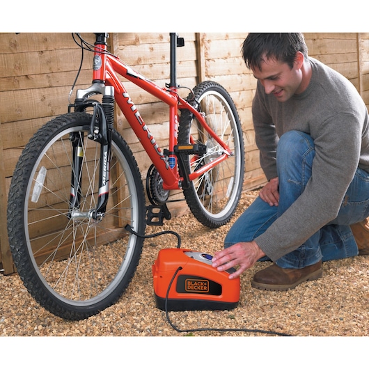 BLACKDECKER ASI300 portable air compressor inflating red mountain bike tire outdoors.
