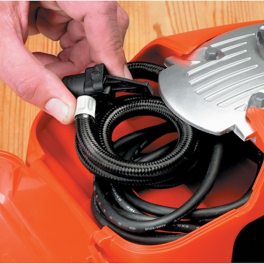 BLACKDECKER ASI300 air compressor hose coiled in orange case with hand holding black nozzle, close-up photography.