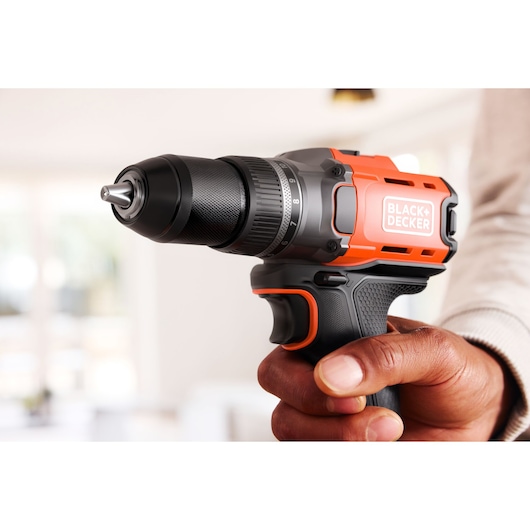 A person holds a BLACK+DECKER cordless drill with an orange and black design, shown in a bright indoor setting.