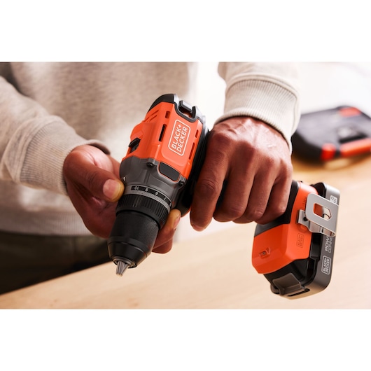 Person holding a BLACK+DECKER cordless drill with orange and black design, preparing for use on a wooden surface.