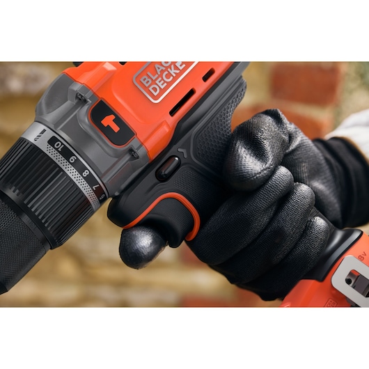 Close-up of a gloved hand holding an orange BLACK+DECKER cordless drill with adjustable settings.