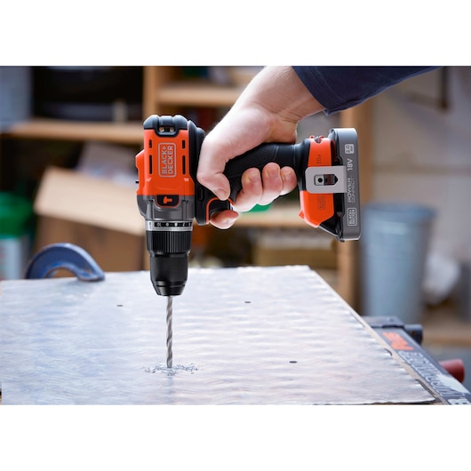 Hand using a BLACK+DECKER cordless drill to make a hole in a metal sheet in a workshop.