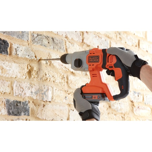 BLACK+DECKER BCD900D1S cordless hammer drill in use on brick wall, close-up side angle.