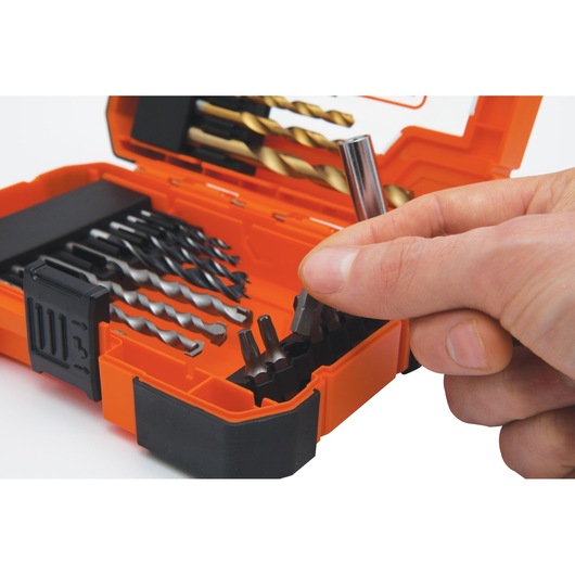 A hand selecting a bit from an orange BLACK+DECKER drill and bit set case containing various drill bits and screwdriver bits.