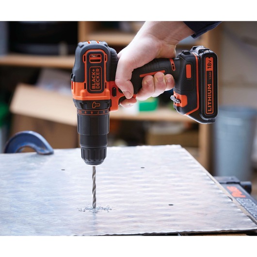 BLACKDECKER BDCHD18 cordless drill in use drilling metal, orange and black color, close-up side angle.