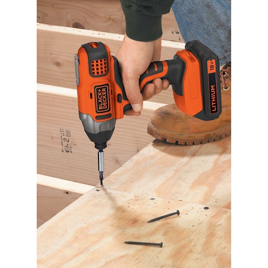 A person uses a BLACK+DECKER 18V lithium cordless impact driver to screw a fastener into plywood during construction.