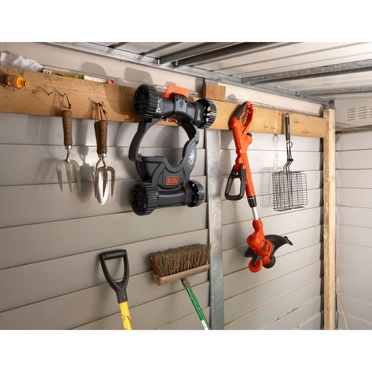 Photo of BLACK+DECKER BESTE630CM trimmer and mower parts hanging on a shed wall with other garden tools.