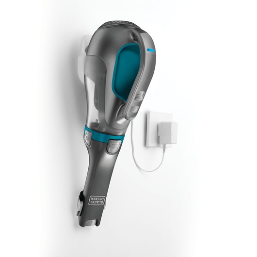 A BLACK+DECKER handheld vacuum cleaner model DV1210N mounted on a wall with its charging adapter plugged into an outlet.