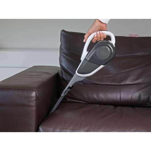 A BLACK+DECKER handheld vacuum cleaner being used to clean between the cushions of a dark brown leather sofa.