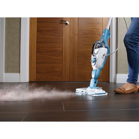 A person using a BLUE and white BLACK+DECKER steam mop to clean a dark tiled floor. Steam is visibly coming out from the mop head.