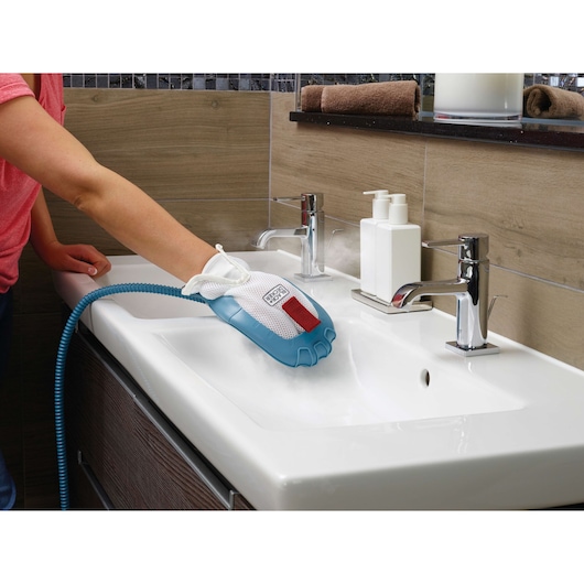 A person using a BLACK+DECKER steam cleaning glove to clean a bathroom sink. The glove emits steam, helping to sanitize and remove dirt from the surface.