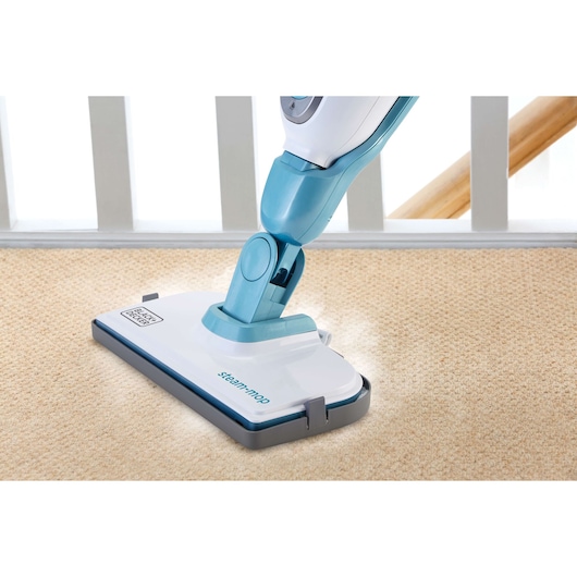 A BLACK+DECKER steam mop is cleaning a light-colored carpet, with part of the mop head visible and steam coming out. The mop has a blue and white design.