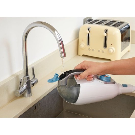 A person fills the water tank of a BLACK+DECKER steam mop under a kitchen faucet. There is a toaster in the background on the countertop.