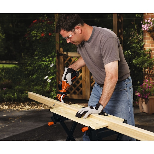 BLACKDECKER GKC108 cordless saw used on wood outdoors, person wearing gloves and safety glasses.