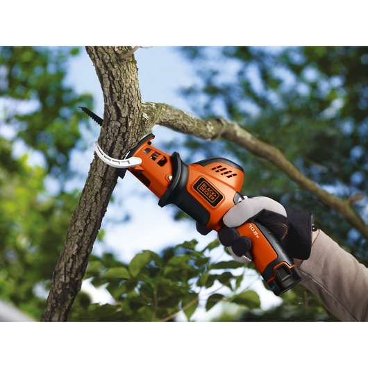 Photo of BLACK+DECKER GKC108 cordless pruning saw cutting a tree branch, gloved hand holding handle outdoors.