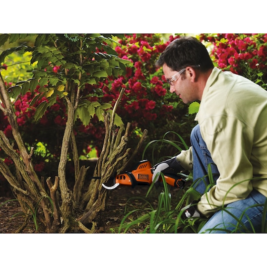 BLACKDECKER GKC108 cordless pruning saw used on tree branches in a garden setting.