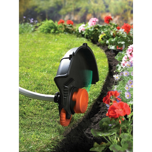 A BLACK+DECKER grass trimmer edging a lawn along a flower bed with blooming flowers and green grass.