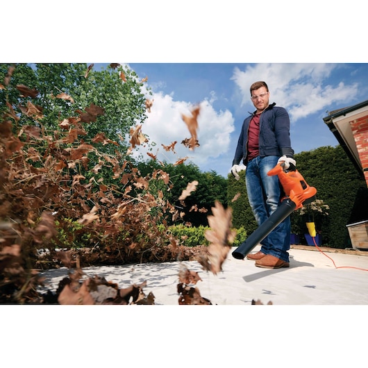 BLACKDECKER GW3050 leaf blower in use outdoors, orange color, blowing dry leaves on patio.