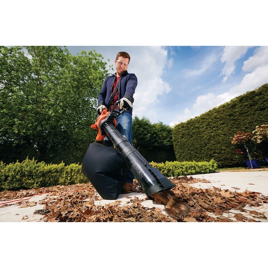 BLACKDECKER GW3050 leaf blower and vacuum in use on dry leaves outdoors with user wearing gloves.