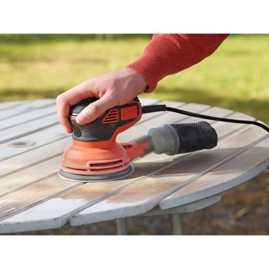 A hand using a BLACK+DECKER KA199 electric sander to sand down a wooden outdoor table.