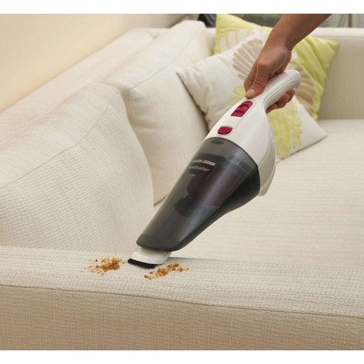 A BLACK+DECKER handheld vacuum cleaner being used to clean crumbs from a light-colored sofa.