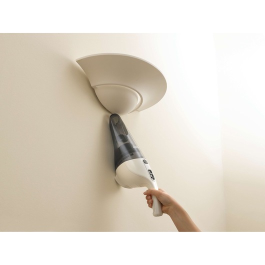 A person using a handheld BLACK+DECKER vacuum cleaner to clean dust from a wall-mounted light fixture.