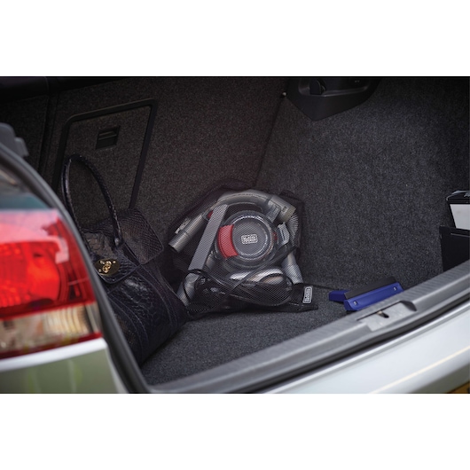 A BLACK+DECKER portable car vacuum cleaner (model PD1200AV) placed in the trunk of a vehicle, next to a black handbag and other items.