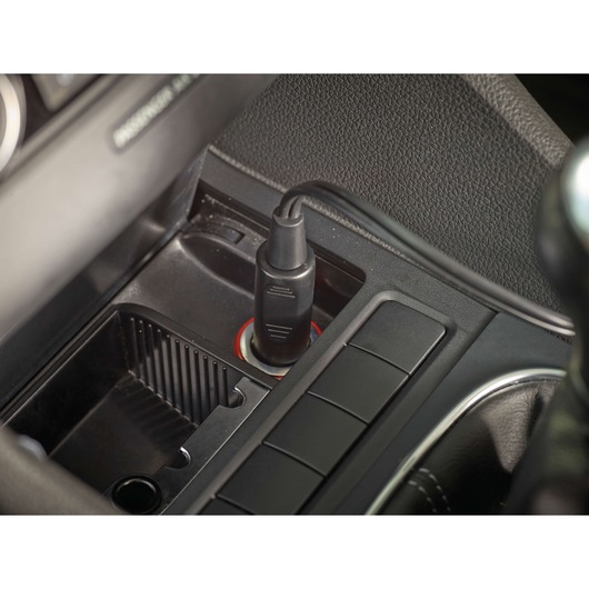 A close-up view of a Black+Decker car accessory plugged into a vehicle's 12V socket, located in the center console area.