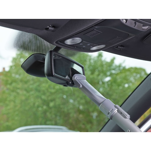 A close-up of a car's interior showing a cleaning brush attached to a telescopic handle being used to clean the rearview mirror.