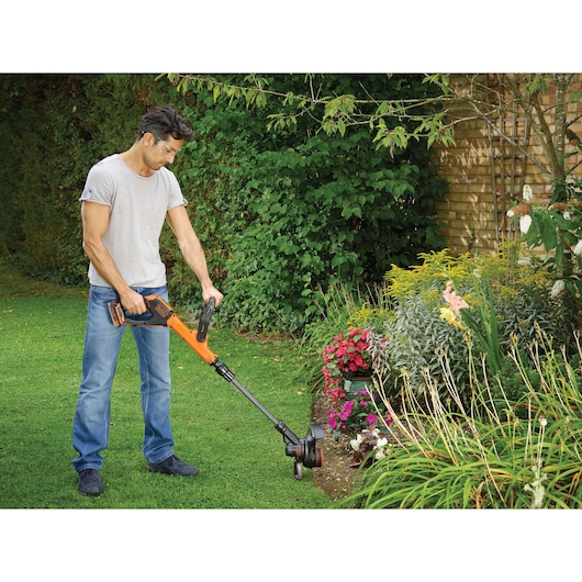 BLACKDECKER STC1820PC grass trimmer used in a garden for edging lawn near flower beds.