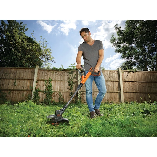 Photo of person using BLACK+DECKER STC1820PC cordless grass trimmer in a garden.