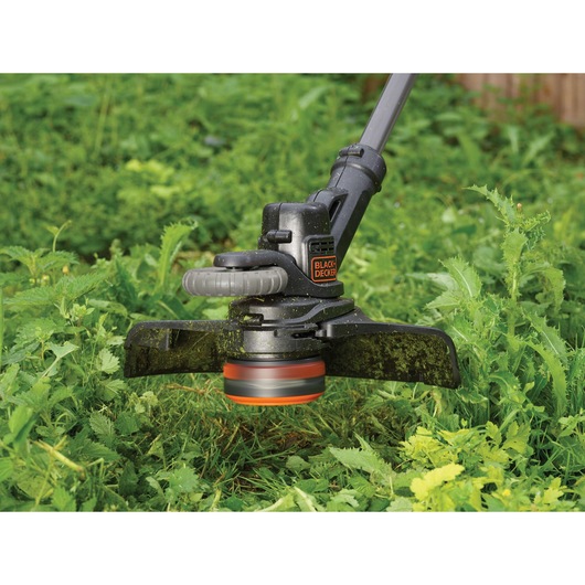 Close-up of a BLACK+DECKER grass trimmer being used to cut overgrown grass and weeds in a garden.